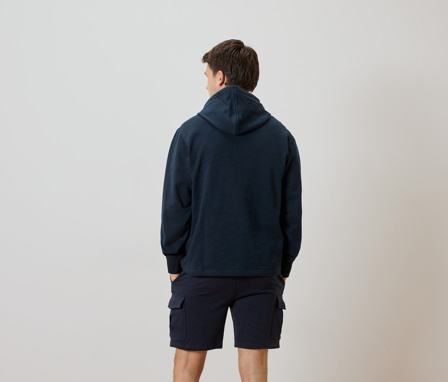 Homme vu de dos portant un sweat à capuche bleu marine et un short.