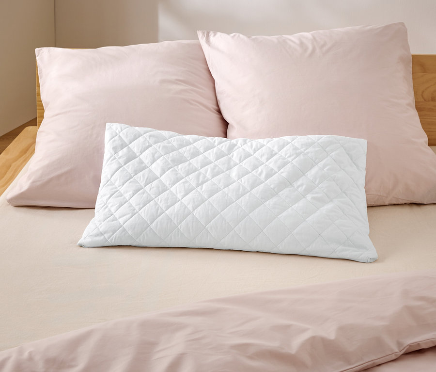 Sur un lit se trouvent deux oreillers roses et un oreiller blanc matelassé.