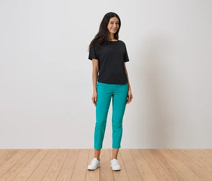 Une femme debout portant un t-shirt noir, un pantalon turquoise et des baskets blanches.