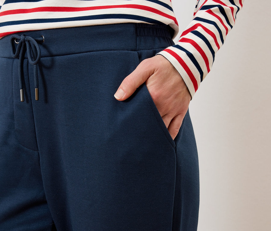 Femme avec la main dans la poche d'un pantalon bleu marine à cordon, portant un haut rayé rouge et blanc.