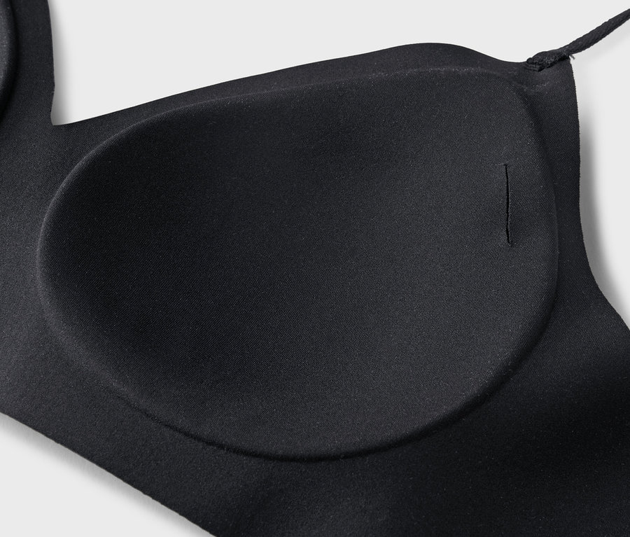 Gros plan d'un soutien-gorge noir avec des bonnets moulés et une fine bretelle sur un fond gris clair.