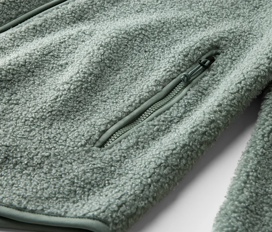 Gros plan d'une veste en polaire vert clair avec une poche zippée.