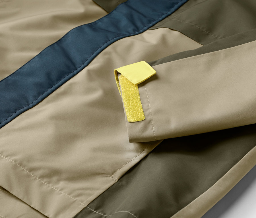 Gros plan sur une veste beige, vert olive et bleu marine avec un détail jaune sur la manche.