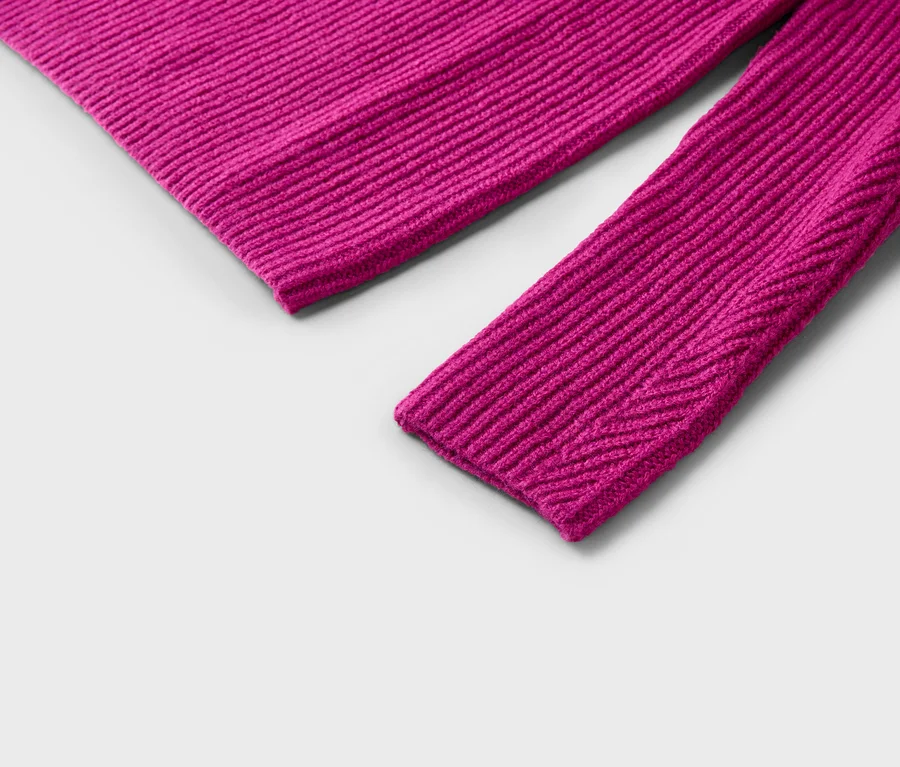 Gros plan sur la manche et une partie du corps d'un pull en tricot côtelé rose sur fond gris.