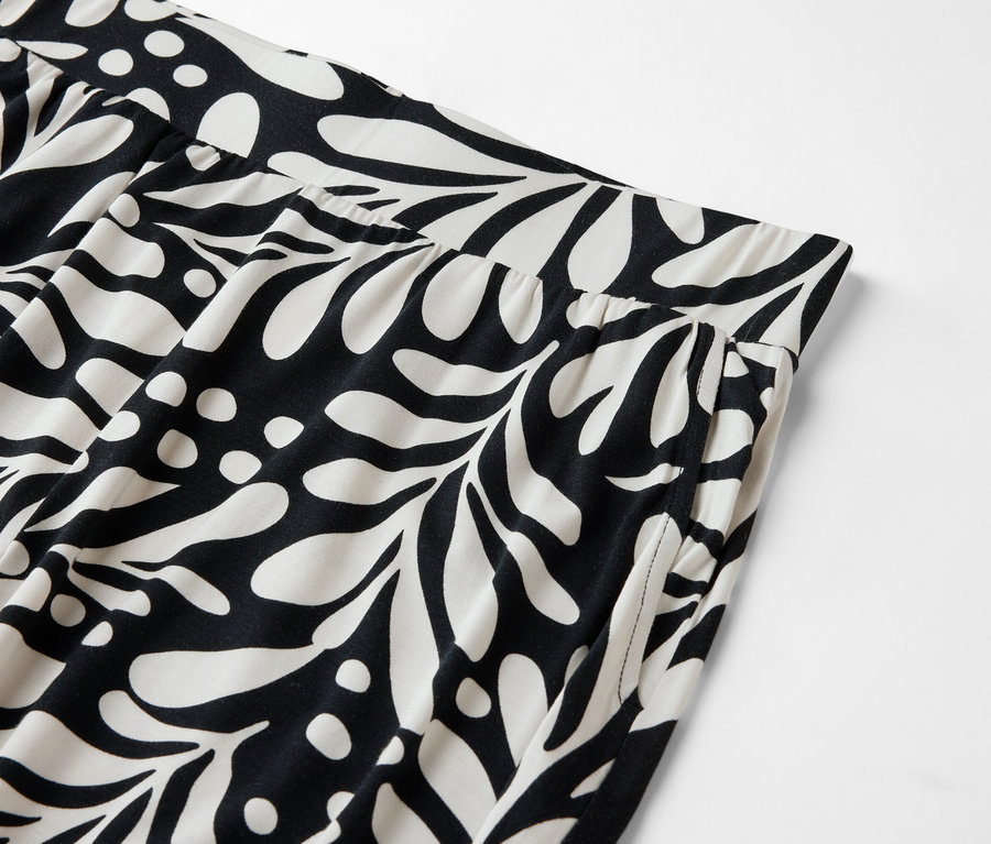 Gros plan d'un pantalon avec une taille élastique et un motif de feuilles noires et de points blancs.