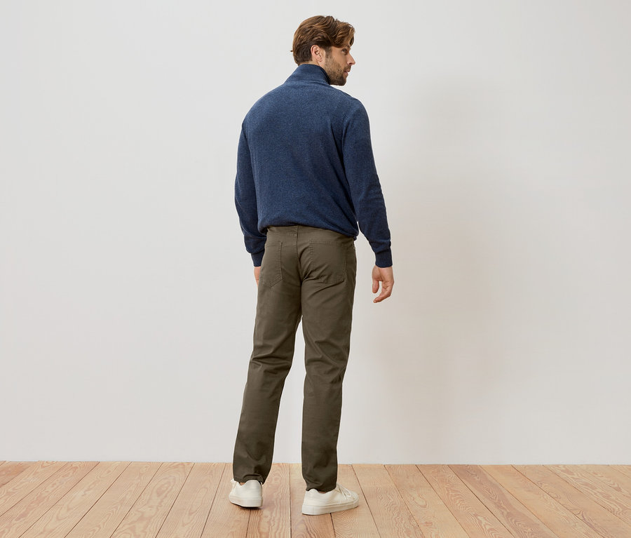 Un homme se tient dos à la caméra, portant un pull bleu marine, un pantalon vert et des baskets blanches.