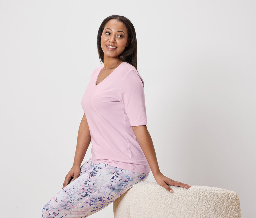 Femme assise sur un tabouret portant un haut rose et un pantalon à motifs.