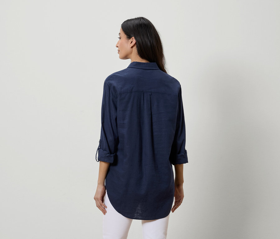 Femme vue de dos portant une chemise bleu marine et un pantalon blanc.
