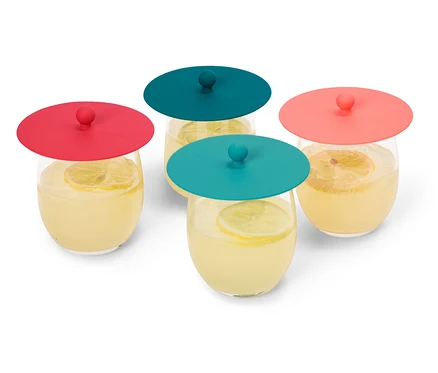 Quatre verres de limonade avec des tranches de citron, recouverts de couvercles en silicone rouges et turquoise, sont posés sur un fond blanc.