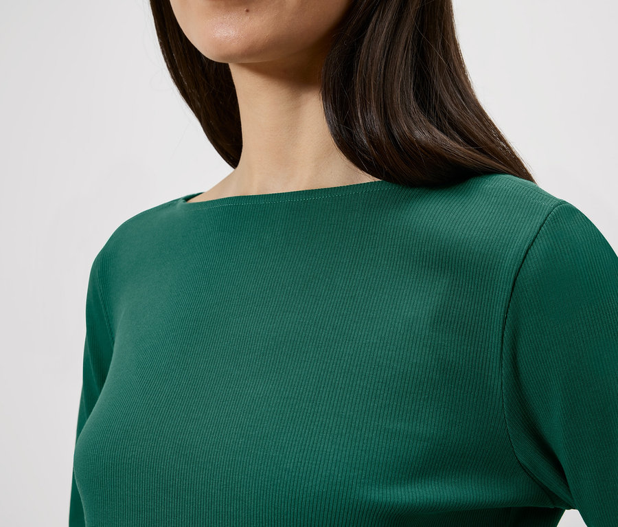 Gros plan d'une femme aux cheveux foncés portant un haut vert à manches longues avec une texture côtelée.