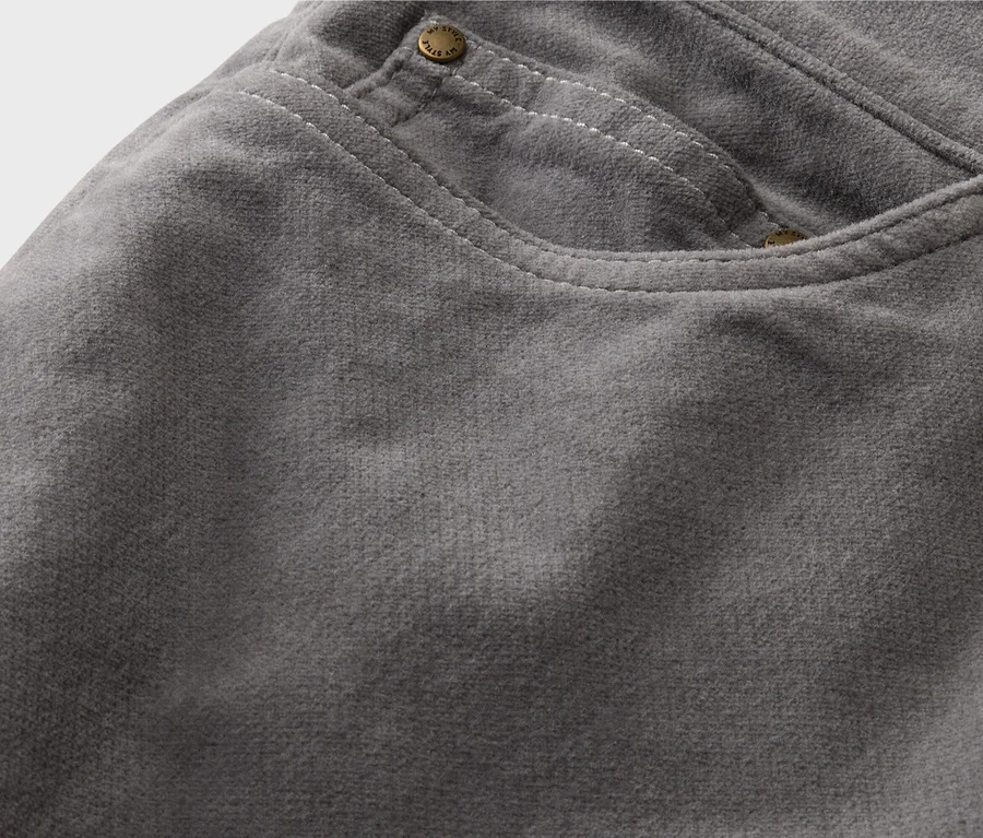 Gros plan sur un pantalon en velours côtelé gris avec une poche, un bouton et des surpiqûres décoratives blanches.