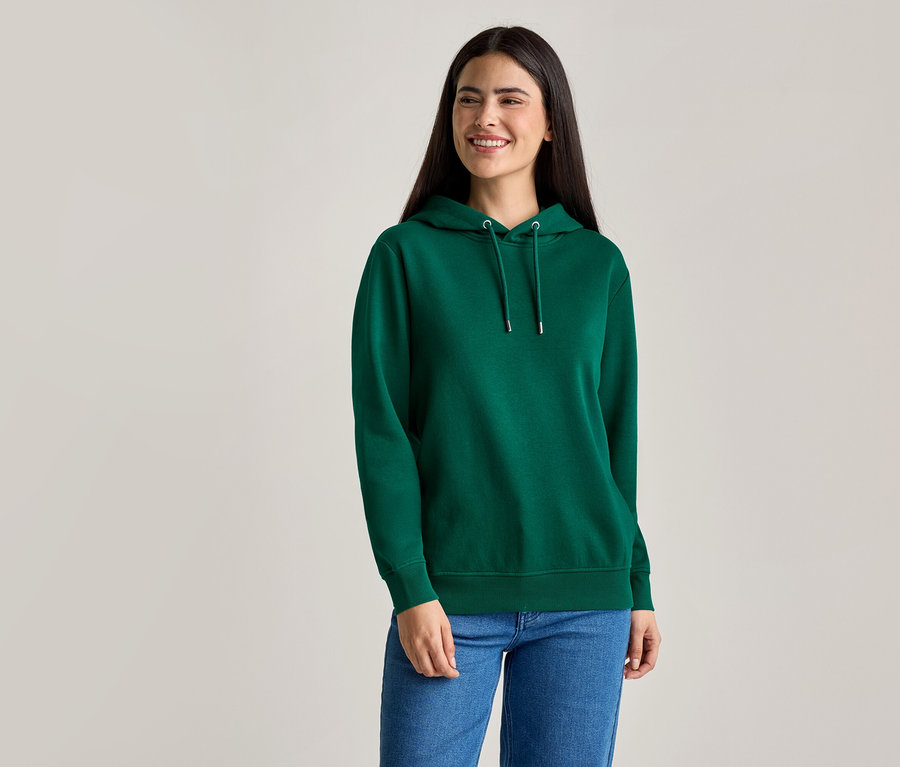 Une femme aux longs cheveux foncés porte un sweat à capuche vert et un jean bleu.