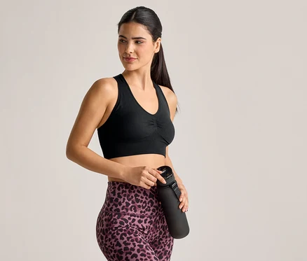 Une femme en brassière de sport et legging à motif léopard tient une bouteille d'eau noire.