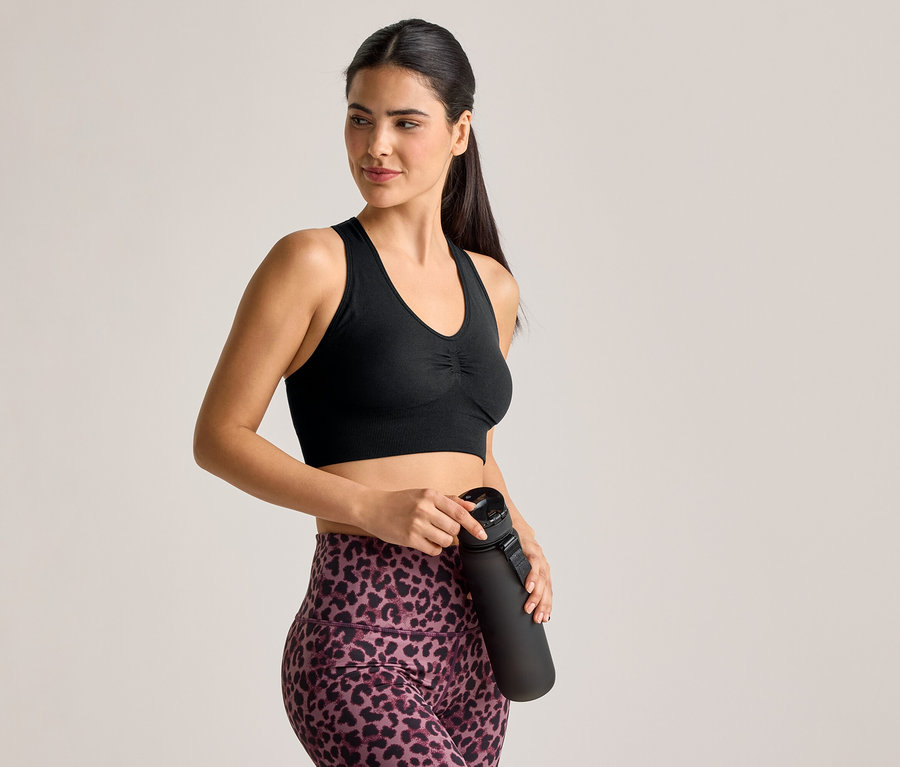 Une femme en brassière de sport et legging à motif léopard tient une bouteille d'eau noire.