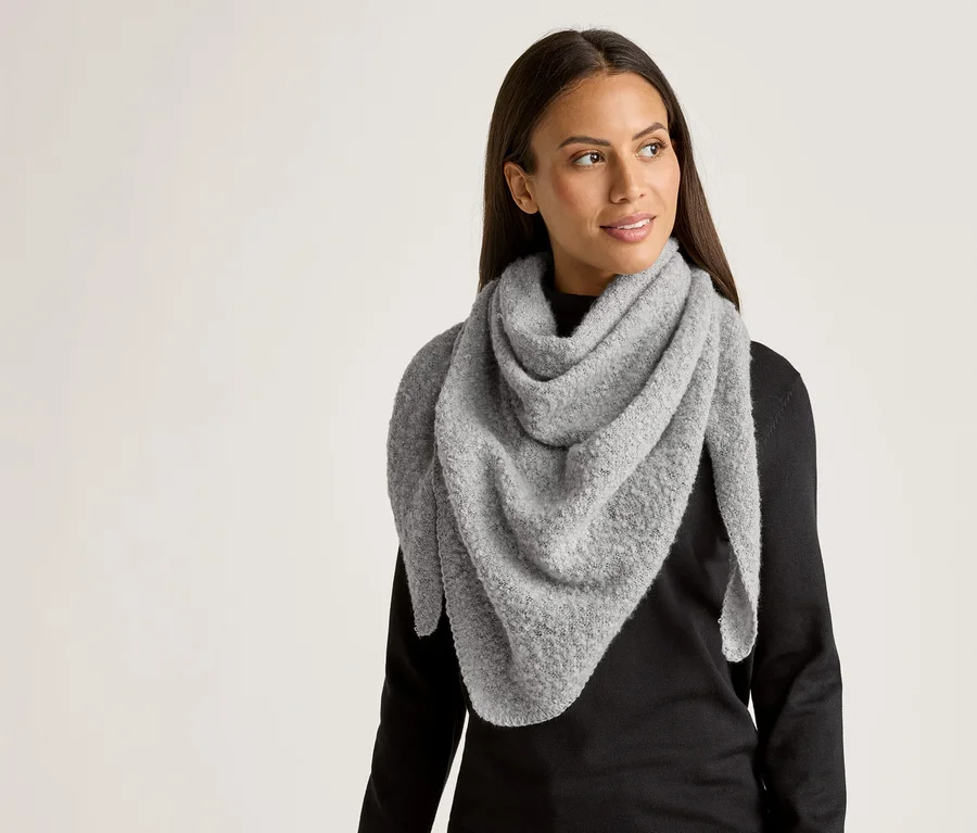 Une femme aux longs cheveux foncés porte un grand châle triangulaire gris clair sur un haut noir.