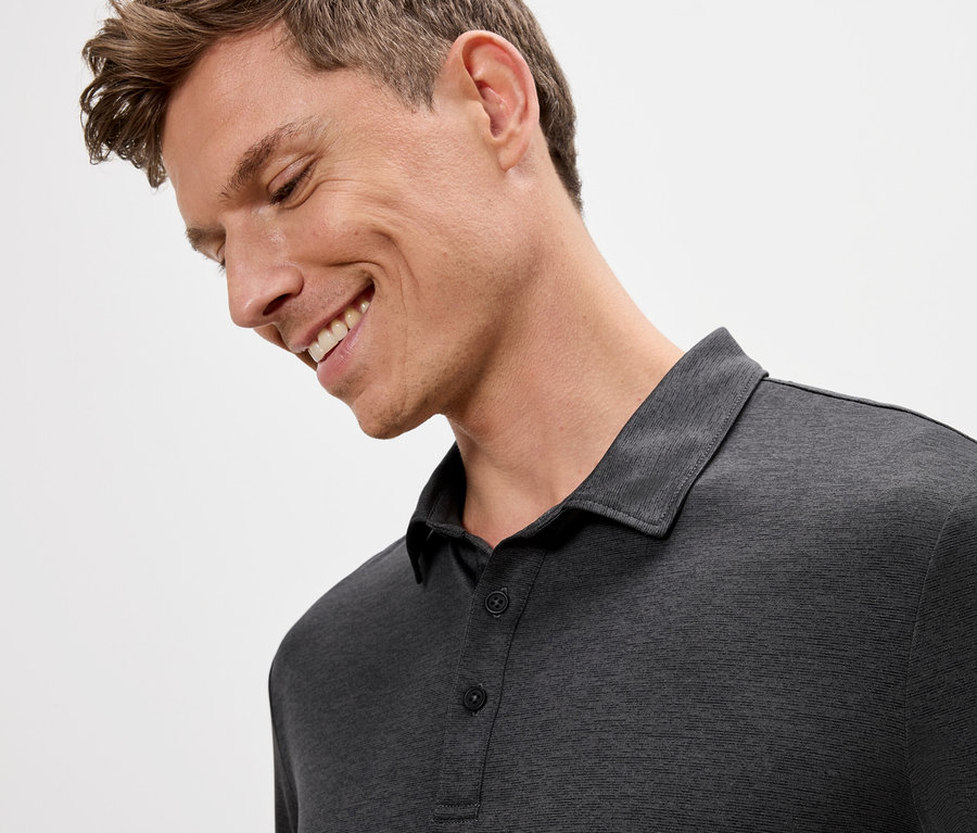 Homme souriant portant un polo gris.