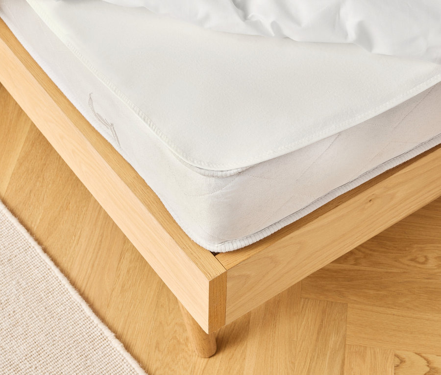 Vue détaillée d'un lit avec un matelas blanc et du linge de lit sur un plancher en bois clair, à côté d'un tapis beige.