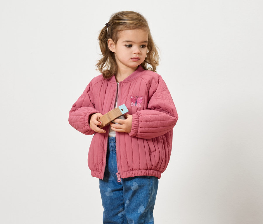 Fille avec une veste rose tenant un jouet en bois.