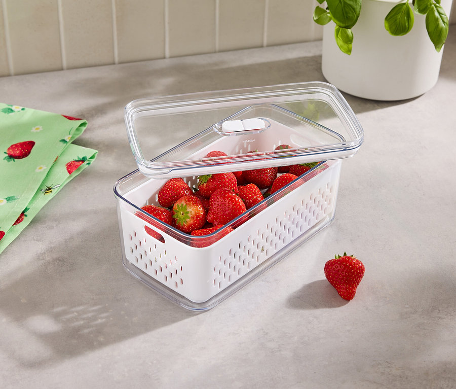 Des fraises dans un récipient de conservation avec un couvercle transparent, à côté d'un torchon à fraises.