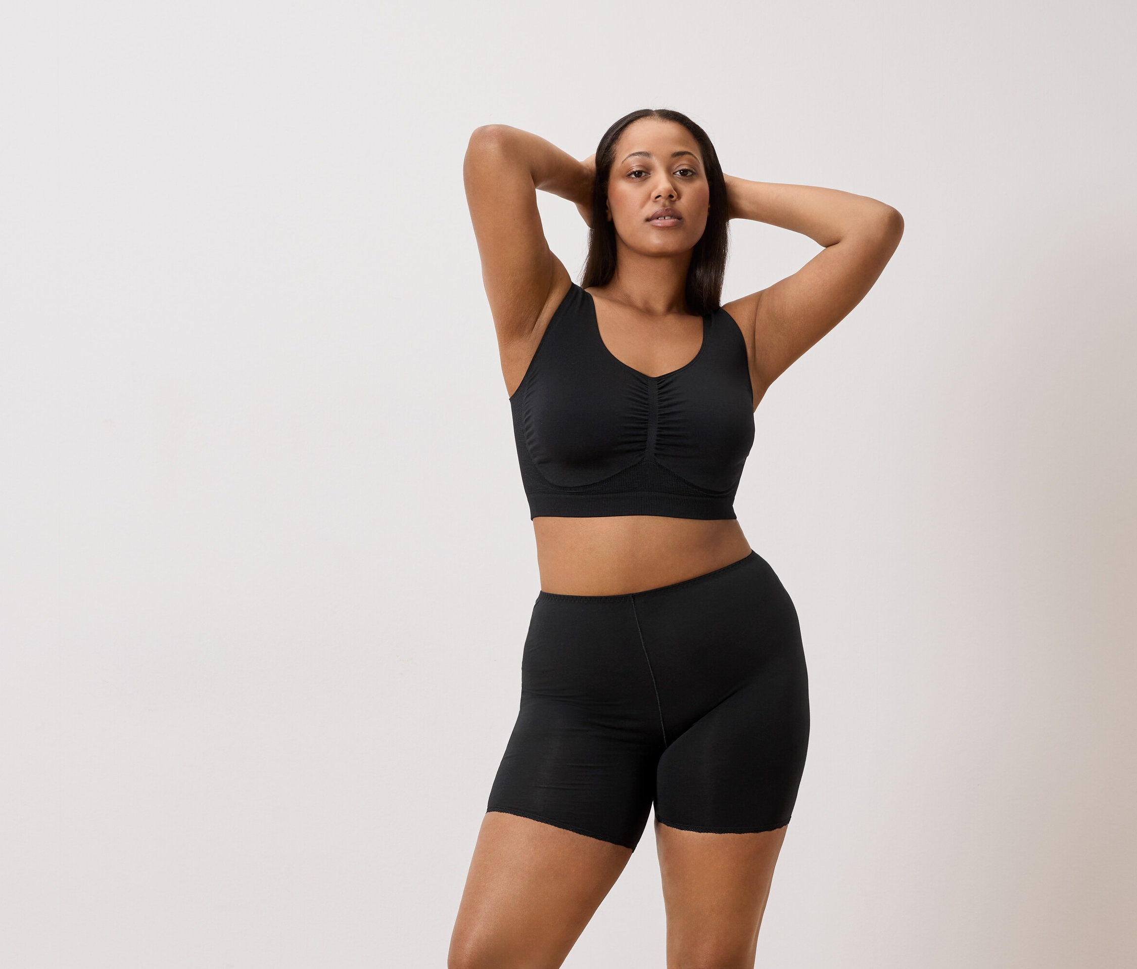 Femme posant en soutien-gorge de sport noir et short noir, les mains jointes derrière la tête.