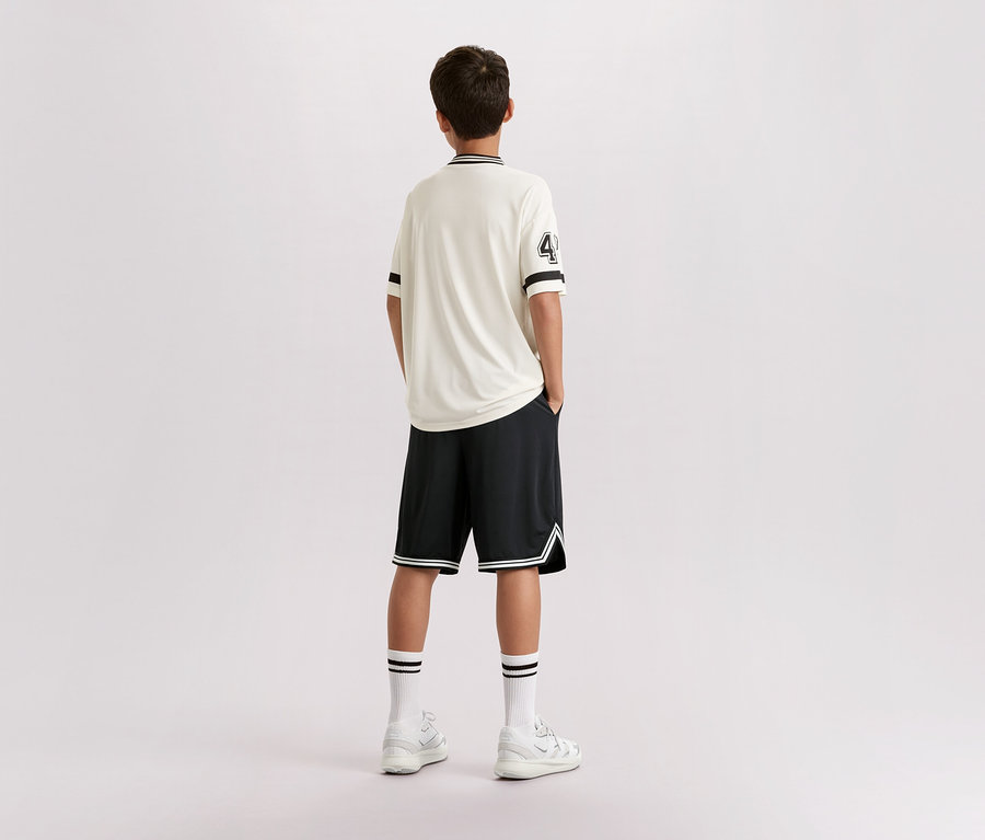 Un jeune homme se tient dos à la caméra, il porte un t-shirt clair avec le numéro 4, un short noir, des chaussettes blanches et des baskets.