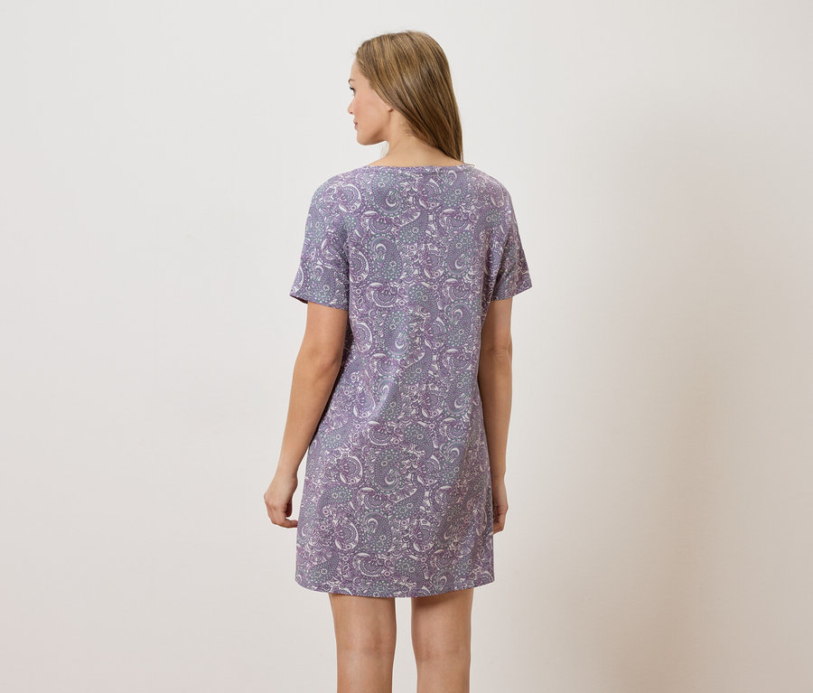 Femme vue de dos portant une robe lilas à motifs à manches courtes sur fond neutre.