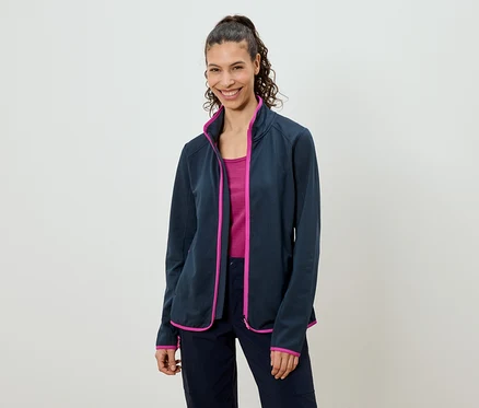 Une femme avec une queue de cheval porte une veste polaire bleu marine avec des touches de rose par-dessus un haut rose et un pantalon bleu marine.