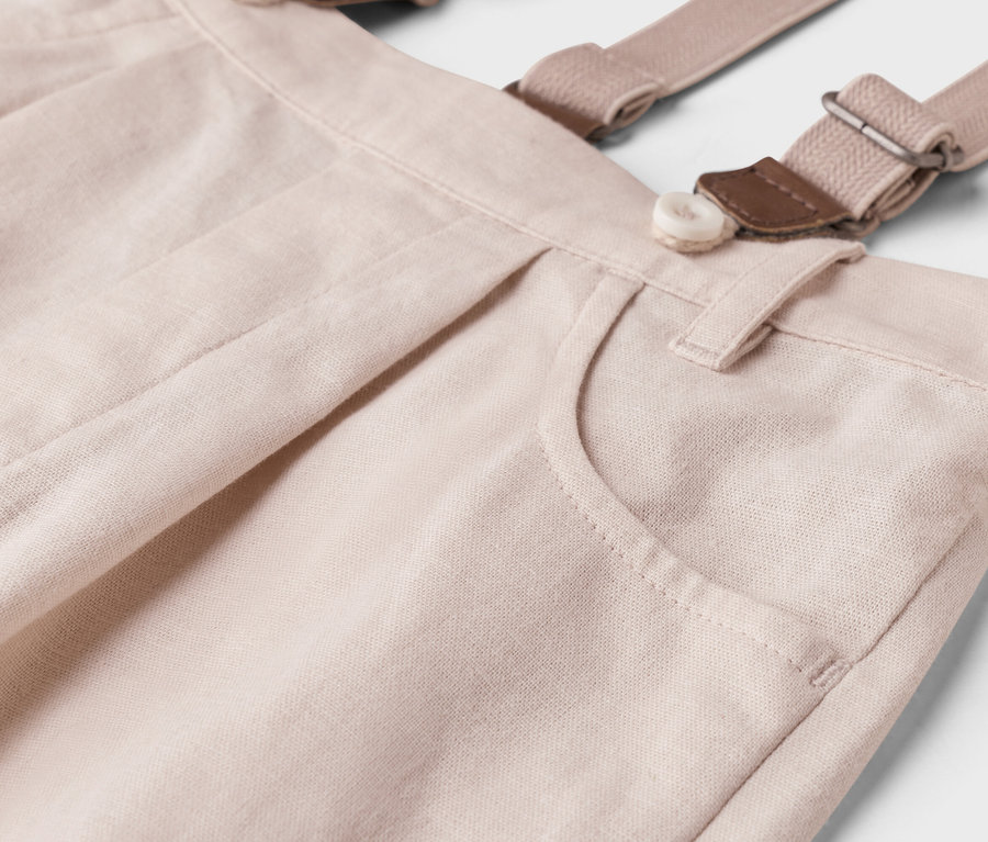 Gros plan d'un pantalon beige clair avec des bretelles, un bouton et une poche.