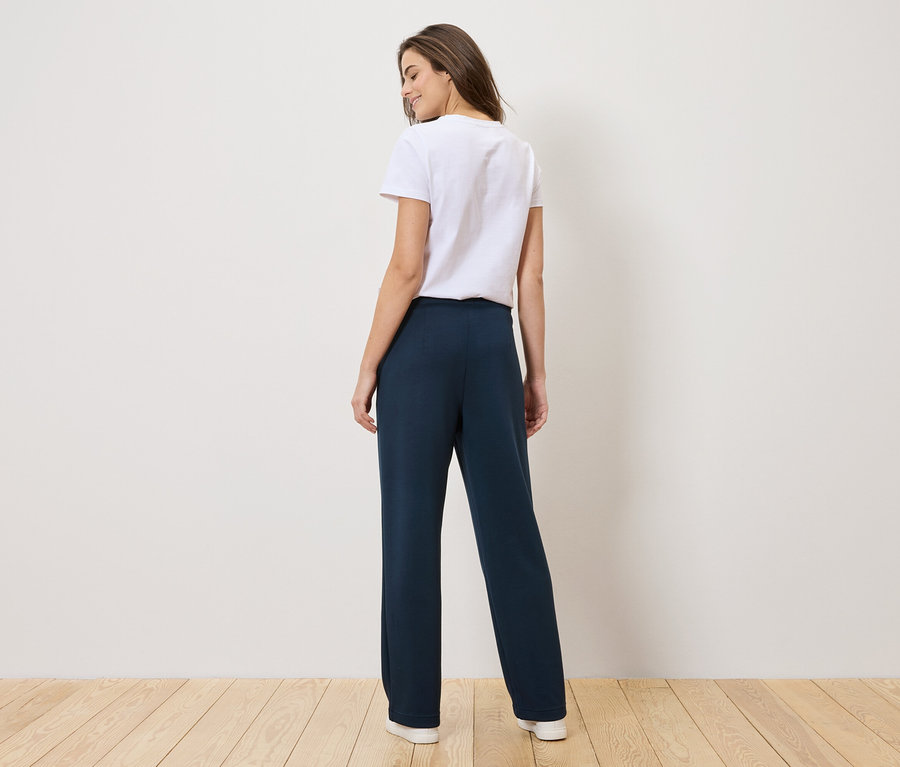 Femme vue de dos portant un t-shirt blanc et un pantalon bleu marine.