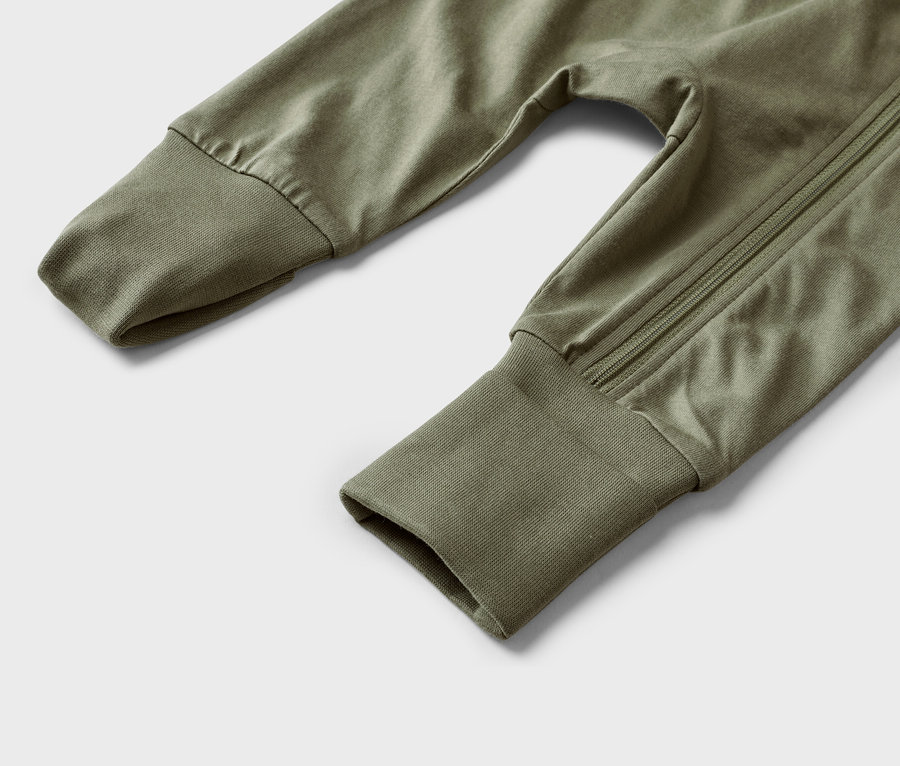 Gros plan d'un pantalon de bébé vert olive avec des poignets aux manches et une fermeture éclair sur le côté.