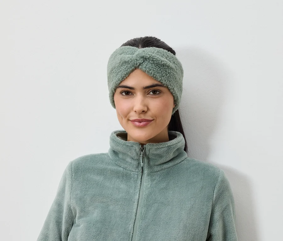 Femme portant un bandeau vert olive et une veste en polaire sur fond blanc.