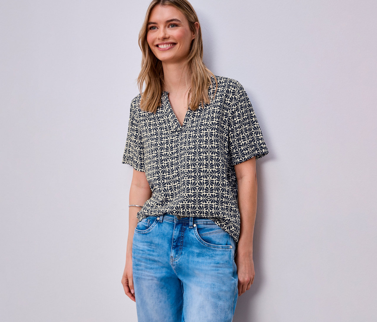 Une femme porte un jean bleu et une blouse en maille Street One à motifs.