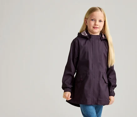 Une fillette aux longs cheveux blonds porte un imperméable aubergine à capuche et un jean bleu.