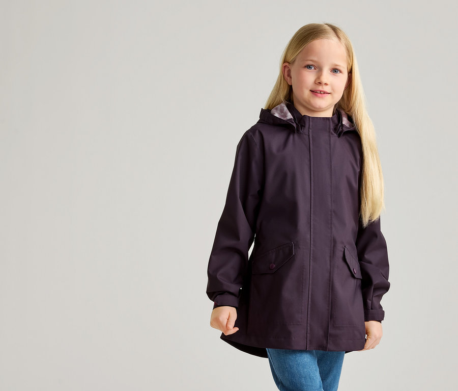 Une fillette aux longs cheveux blonds porte un imperméable aubergine à capuche et un jean bleu.