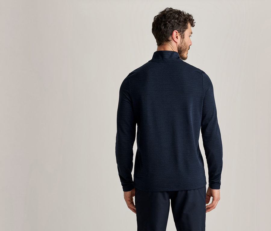 Homme de dos portant un haut à manches longues bleu foncé et un pantalon bleu foncé devant un fond clair.