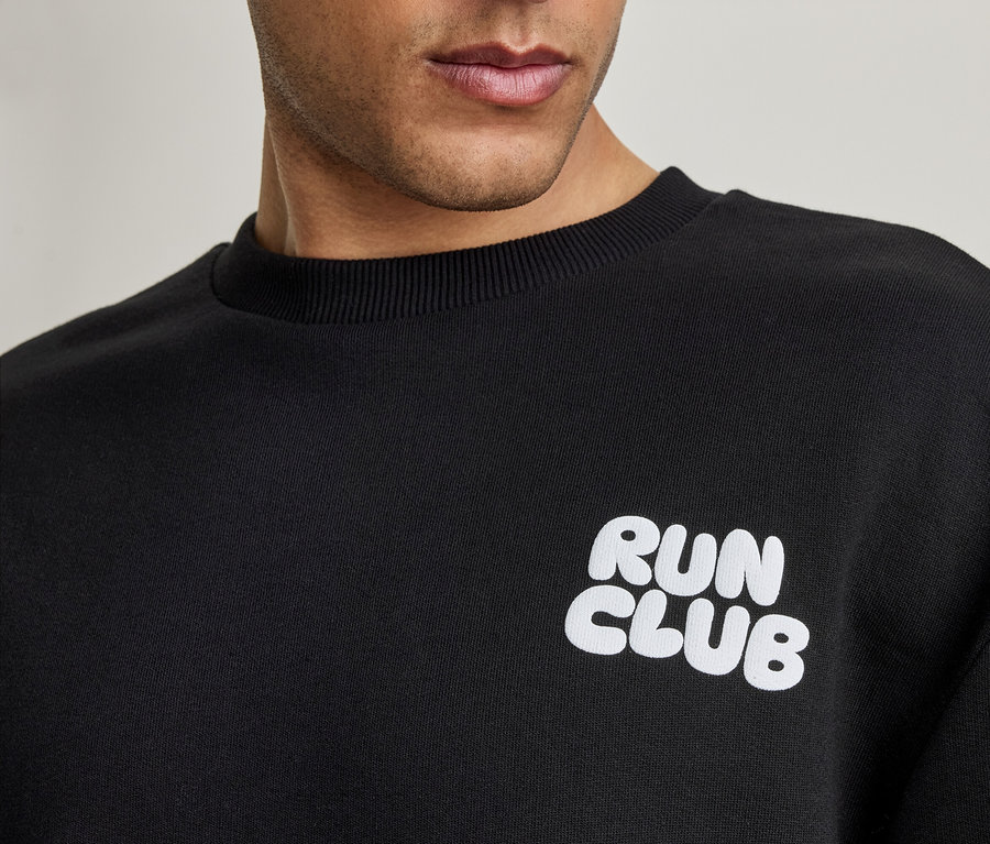 Gros plan d'un homme portant un sweatshirt noir avec l'inscription blanche 'RUN CLUB'.