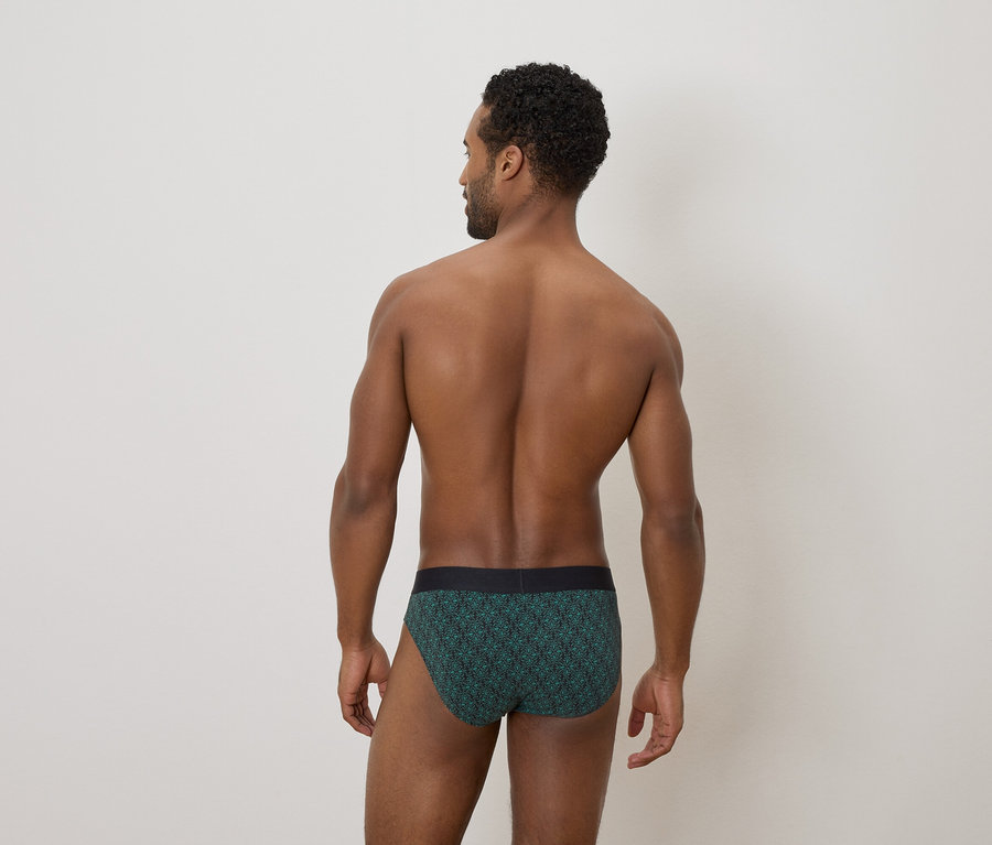 Vue arrière d'un homme à la peau foncée et aux cheveux bouclés portant un slip vert à motifs.
