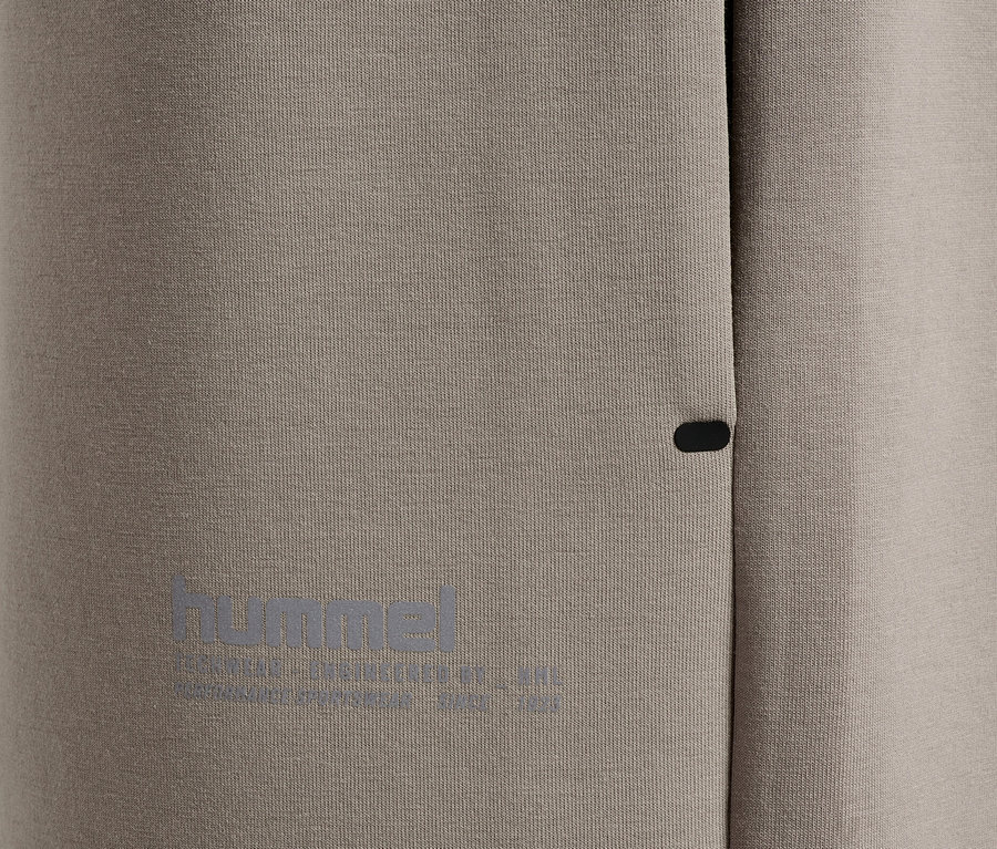 Gros plan de vêtements de sport gris avec un petit bouton foncé et un logo "hummel" réfléchissant.