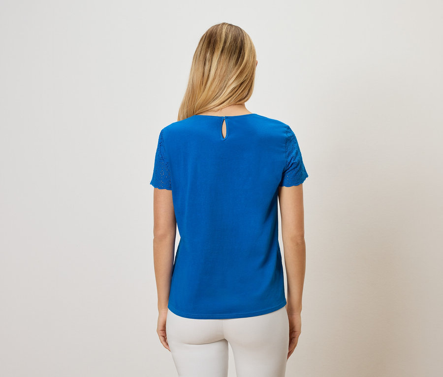 Vue arrière d'une femme aux longs cheveux blonds portant un t-shirt bleu et un pantalon blanc.