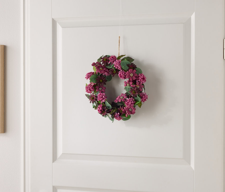 Petite couronne florale avec des fleurs violettes et des feuilles vertes suspendue à une porte blanche.