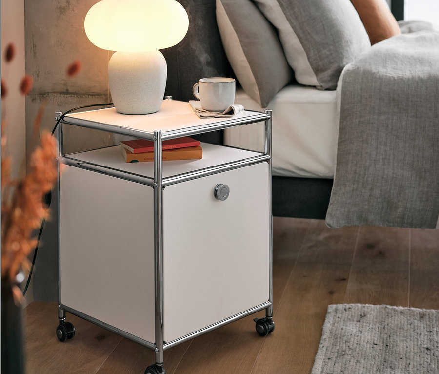 Lampe de table avec abat-jour en verre sur caisson en métal à roulettes « CN3 » avec abattant, blanc, à côté du lit.