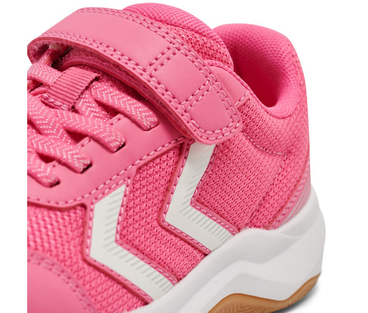 Gros plan d'une chaussure de sport rose. Elle présente un matériau en maille rose, des rayures chevrons blanches sur le côté, des lacets roses en zigzag et une sangle velcro rose sur les lacets. La semelle est blanche avec un dessous marron.
