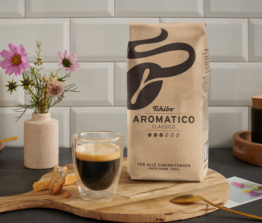 Une tasse de café est posée à côté d'un paquet d'Aromatico Classico - 1 kg Ganze Bohne sur une table en bois.