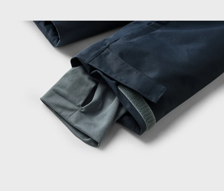 Gros plan d'une manche de veste bleu foncé avec un poignet intérieur gris doté d'un trou pour le pouce et une sangle velcro grise sur la manche extérieure.