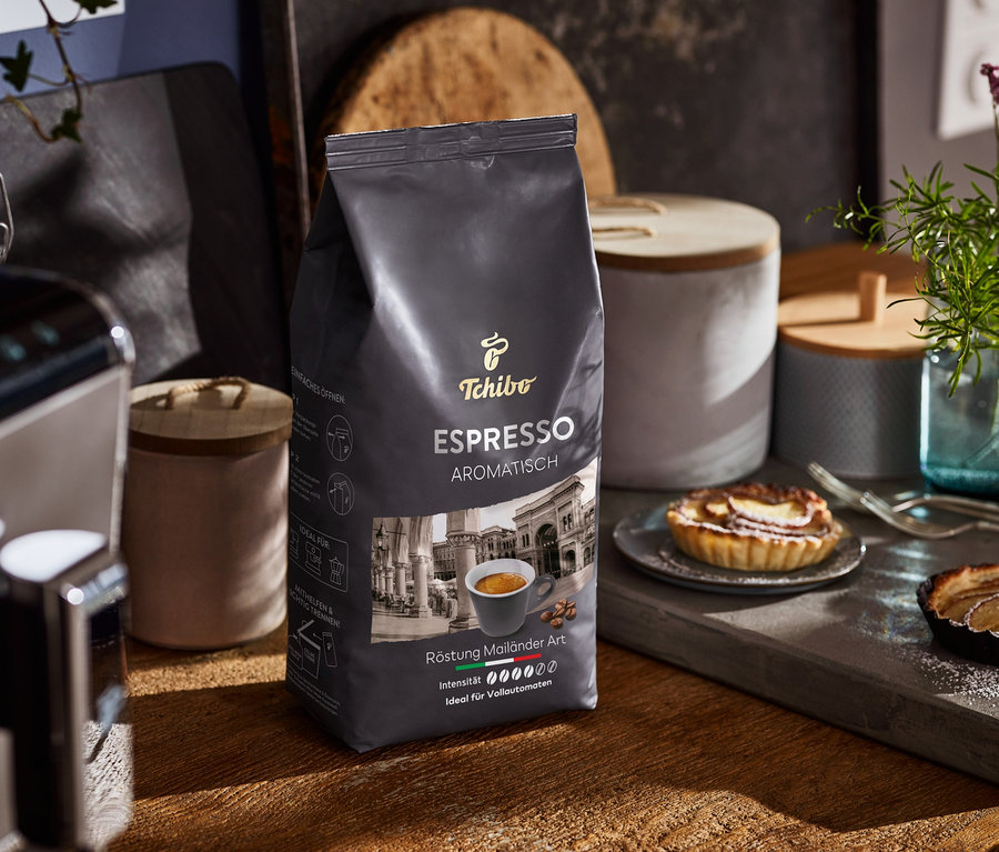 Un paquet d'Expresso aromatique est posé sur une table en bois à côté d'une machine à café et d'assiettes avec des gâteaux.