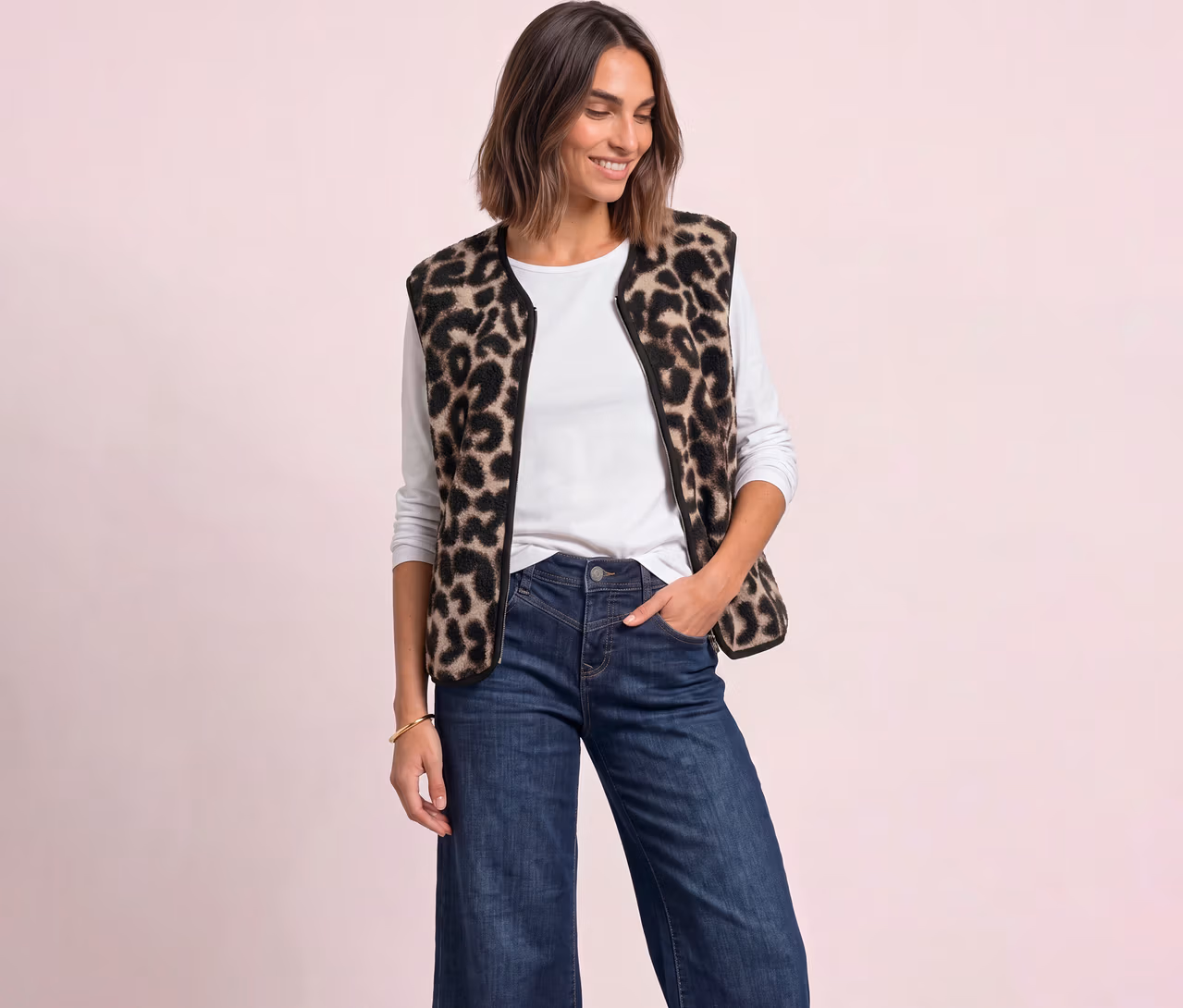 Femme souriante portant un gilet Street One imprimé léopard, un t-shirt blanc à manches longues et un jean bleu, la main dans la poche.