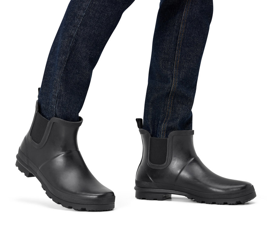 Jambes en jean bleu foncé et bottes de pluie Chelsea noires sur fond blanc.