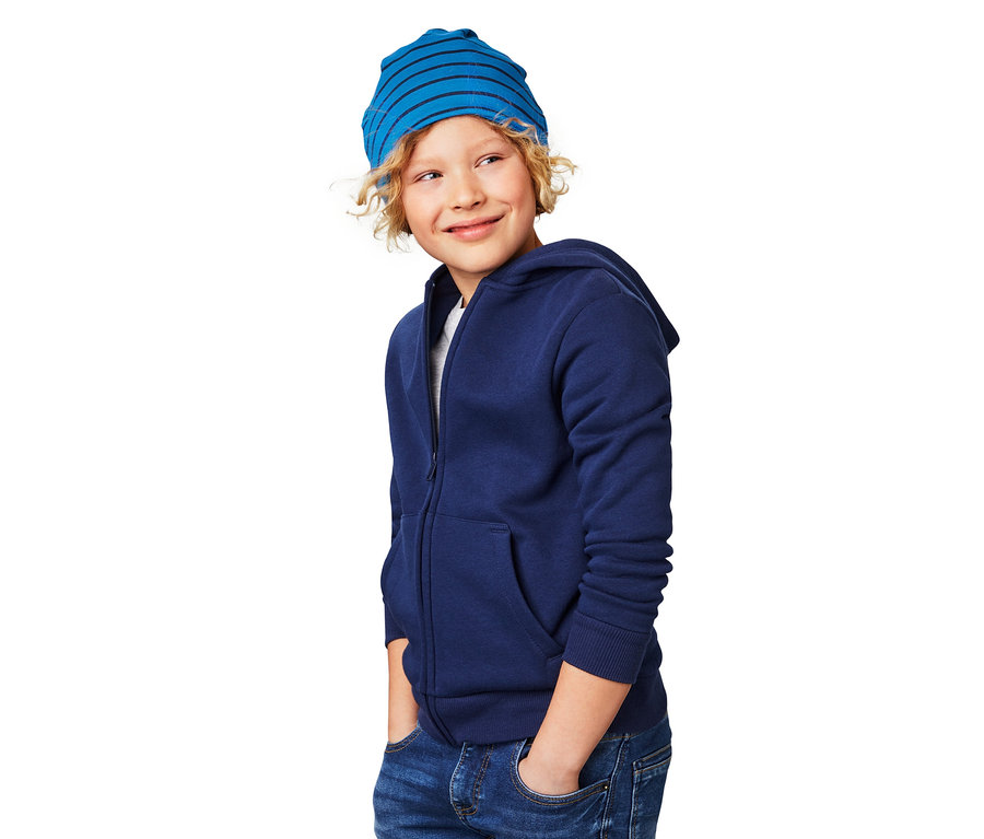 Un garçon blond porte un bonnet réversible bleu et un sweat-shirt zippé bleu.
