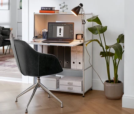 Chaise pivotante rembourrée en similicuir devant un secrétaire métal «
CN3
» blanc avec lampe à pince.