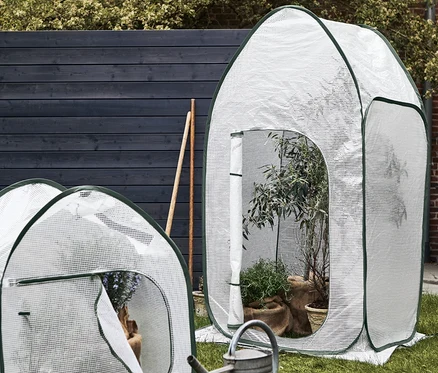 Une haute et une petite serre pop-up pour protéger les plantes sont posées sur une pelouse.